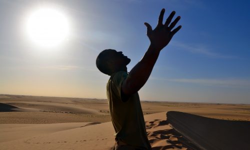 Man experiencing the freedom of the Sahara Desert as the sun looms above his head. Sir Driver Tours. Private tour.